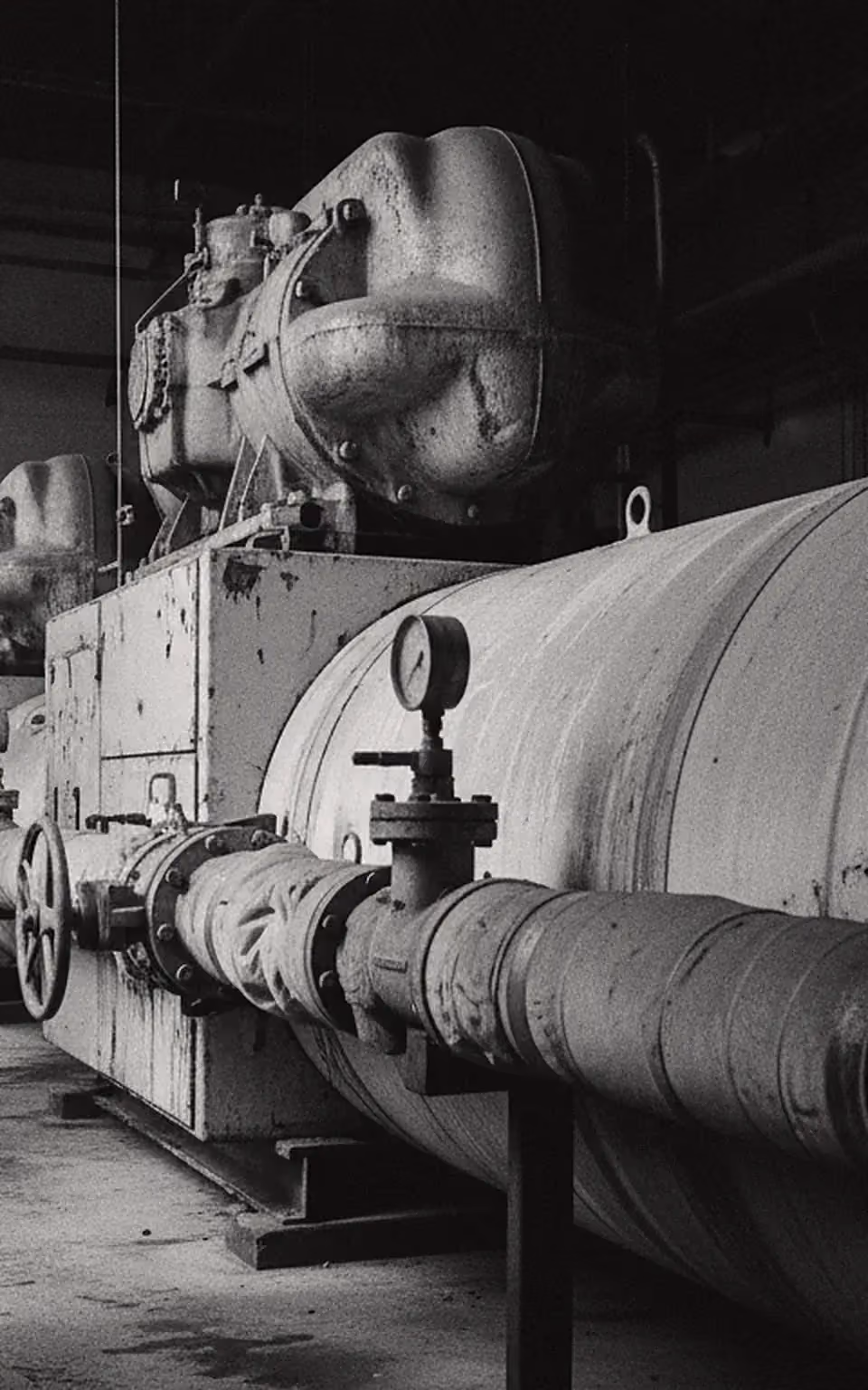 A water-cooled chiller in a hospital central plant, hard window light across its shell and gauge.