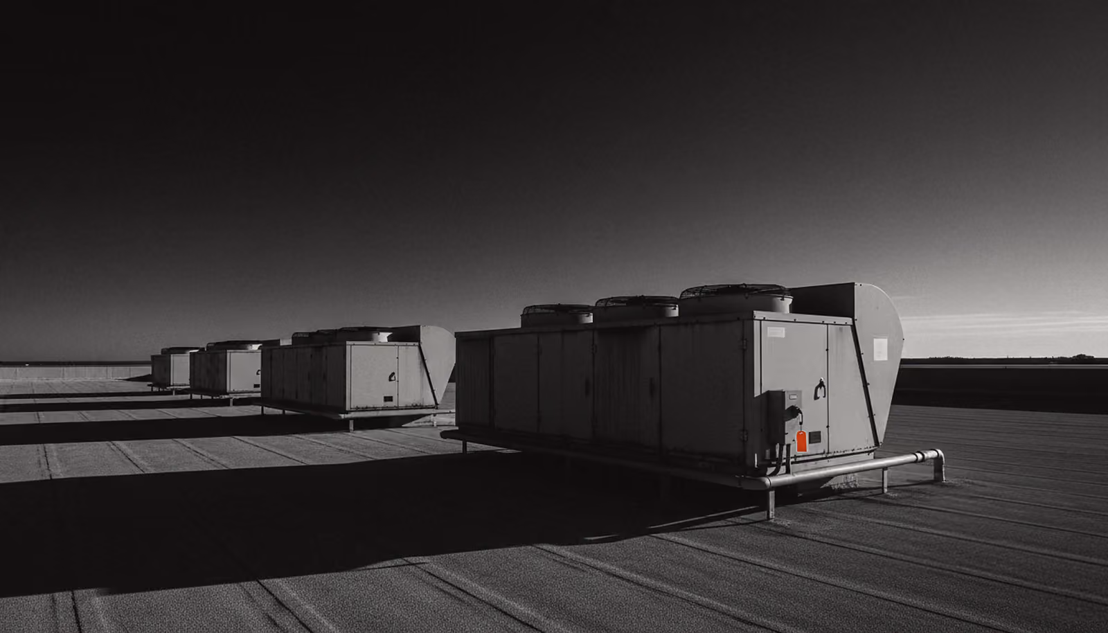 Packaged rooftop units on a hospital roof at first light, an orange lockout tag on the nearest one.